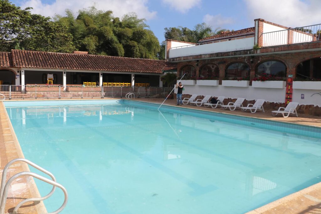 Piscina al aire libre rodeada de tumbonas blancas y una construcción de estilo rústico.