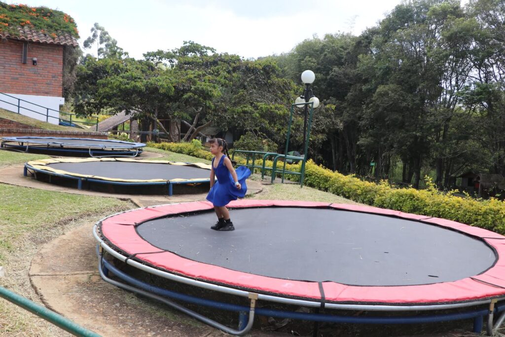 Niña con vestido azul saltando en un trampolín grande al aire libre
