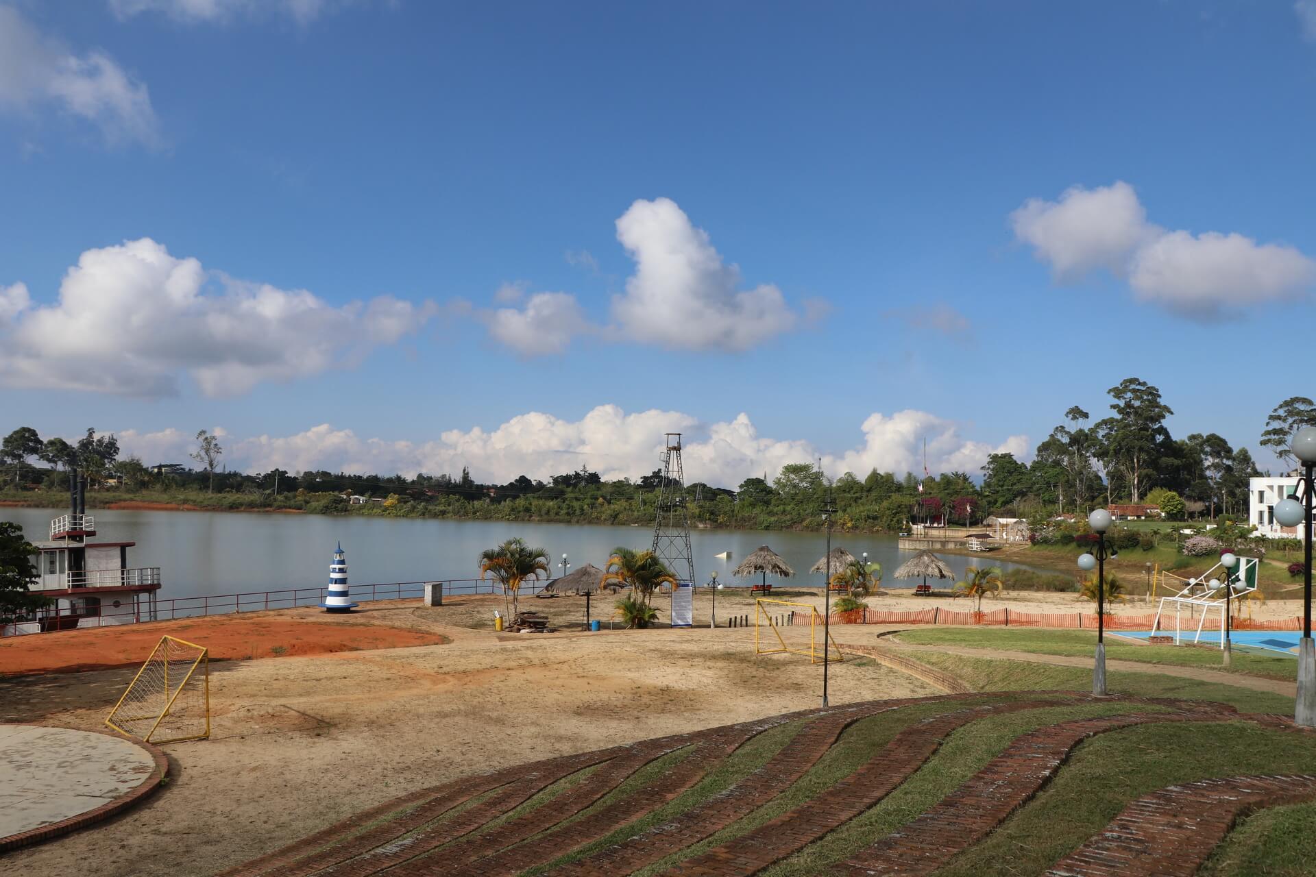 Parque recreativo junto a un lago con cabañas, farolas y áreas verdes.