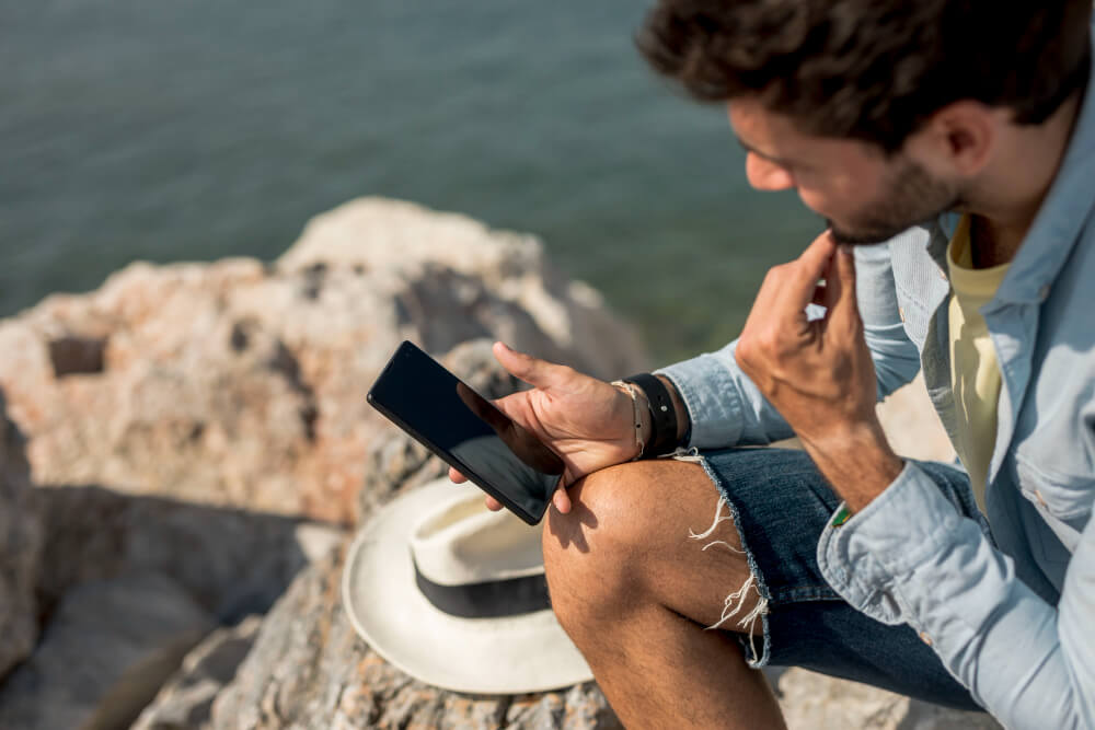 Hombre usando su teléfono móvil mientras descansa cerca del agua