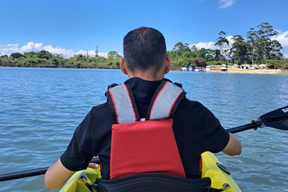 Persona remando en kayak sobre un lago con chaleco salvavidas y paisaje natural al fondo