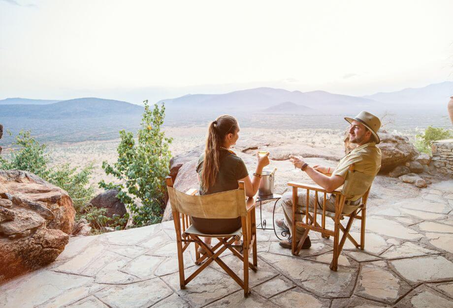 Pareja sentada al aire libre brindando con bebidas mientras disfruta de una vista panorámica de montañas